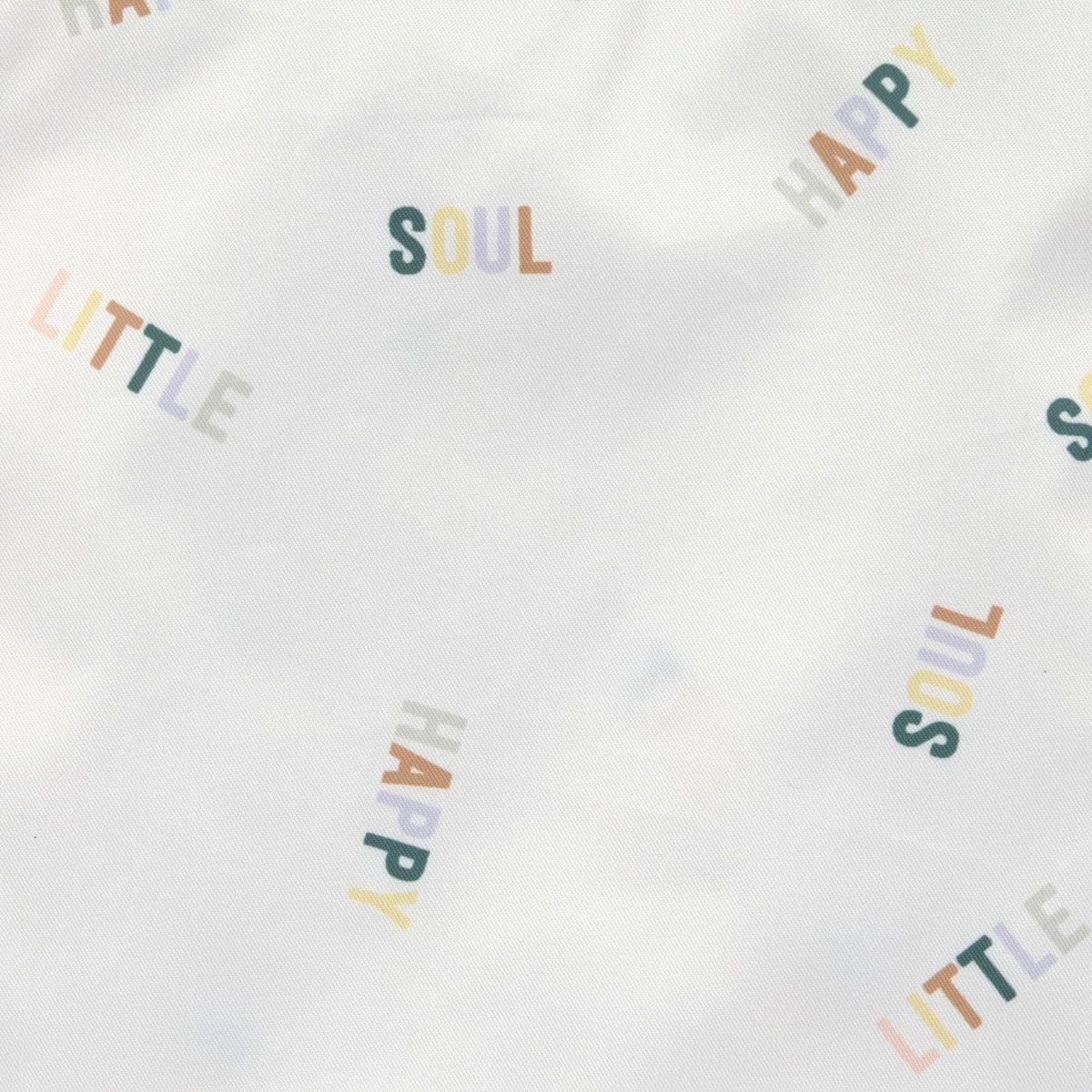 Zbliżenie jasnego materiału torby LÄSSIG z kolorowymi napisami „HAPPY LITTLE SOUL”.
