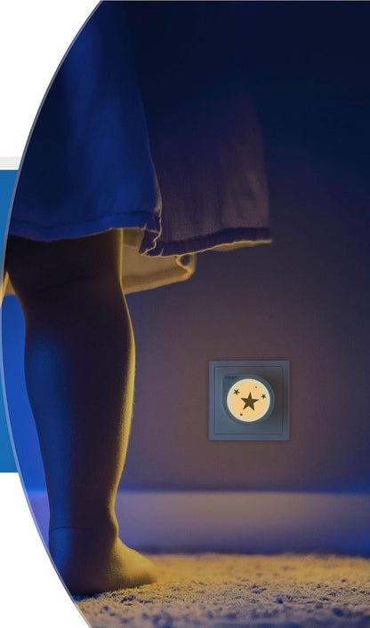 Lampka Reer NightGuide Star świecąca w gniazdku przy podłodze; w kadrze nogi osoby.