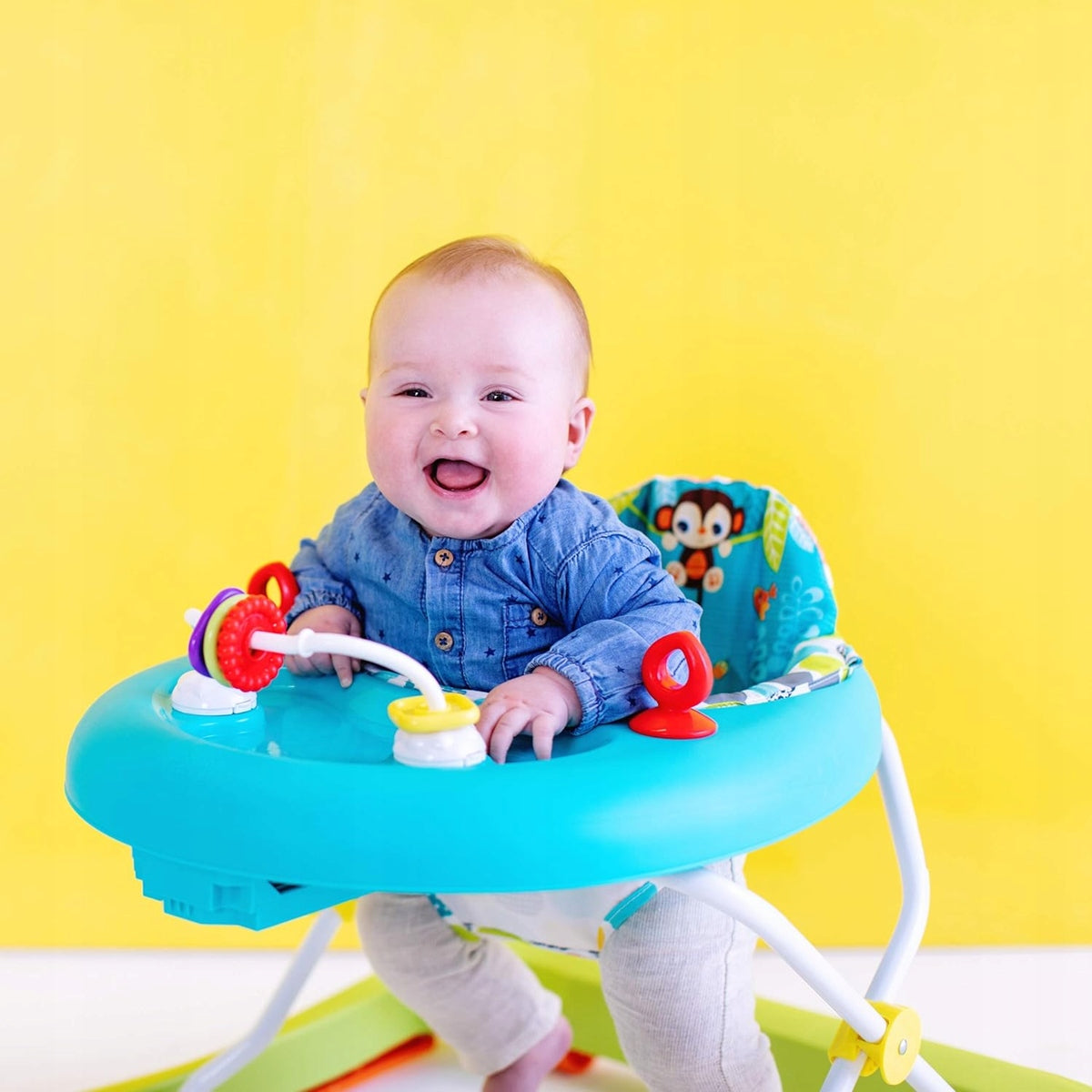 Dziecko przy turkusowej tacy chodzika Bright Starts Giggling Safari na żółtym tle.