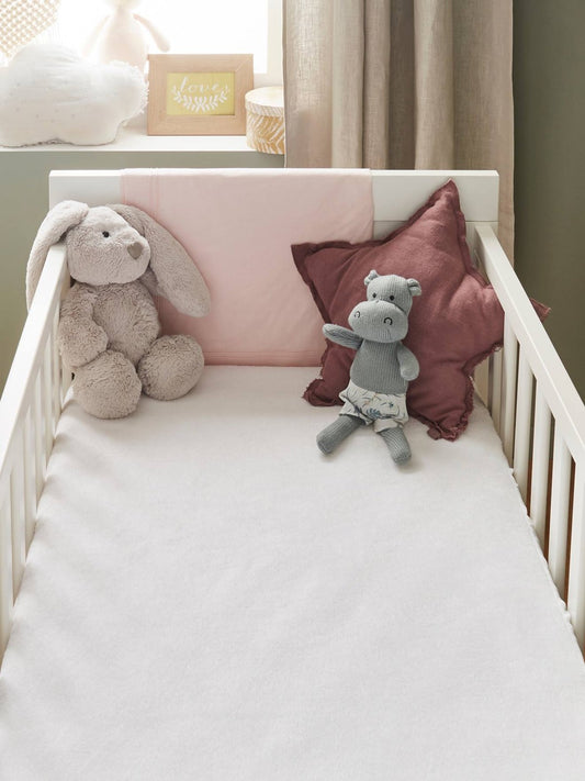 Biały ochraniacz P’tit Lit Bamboo na materacu w łóżeczku, z poduszkami i maskotkami w tle.